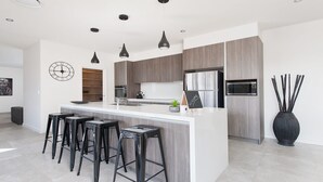 Une cuisine moderne avec un îlot central, des tabourets de bar, une horloge et un panneau d’accueil.