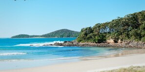 Una spiaggia con acque cristalline, una riva sabbiosa e una collina ricoperta di boschi sullo sfondo.