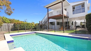 Piscina residencial con un área de terraza techada, una escalera que lleva al segundo piso y un patio trasero cercado.