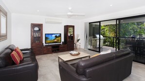 A modern living room with a flat-screen TV, leather sofas, a coffee table, and a balcony with a grill. - 8 Springfield Avenue (Coolum Beach)