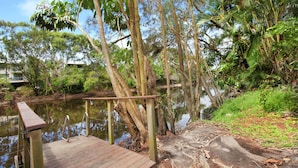 A wooden dock extending over a calm body of water, surrounded by lush greenery and trees. - 8 Springfield Avenue (Coolum Beach)