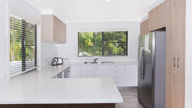 A modern kitchen with white cabinetry, a stainless steel refrigerator, and a window with blinds. - 8 Springfield Avenue (Coolum Beach)