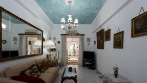 A living room with a sofa, a coffee table, a TV, a chandelier, and framed artwork on the walls. - Garden Central Athinian Apartments (Athens)