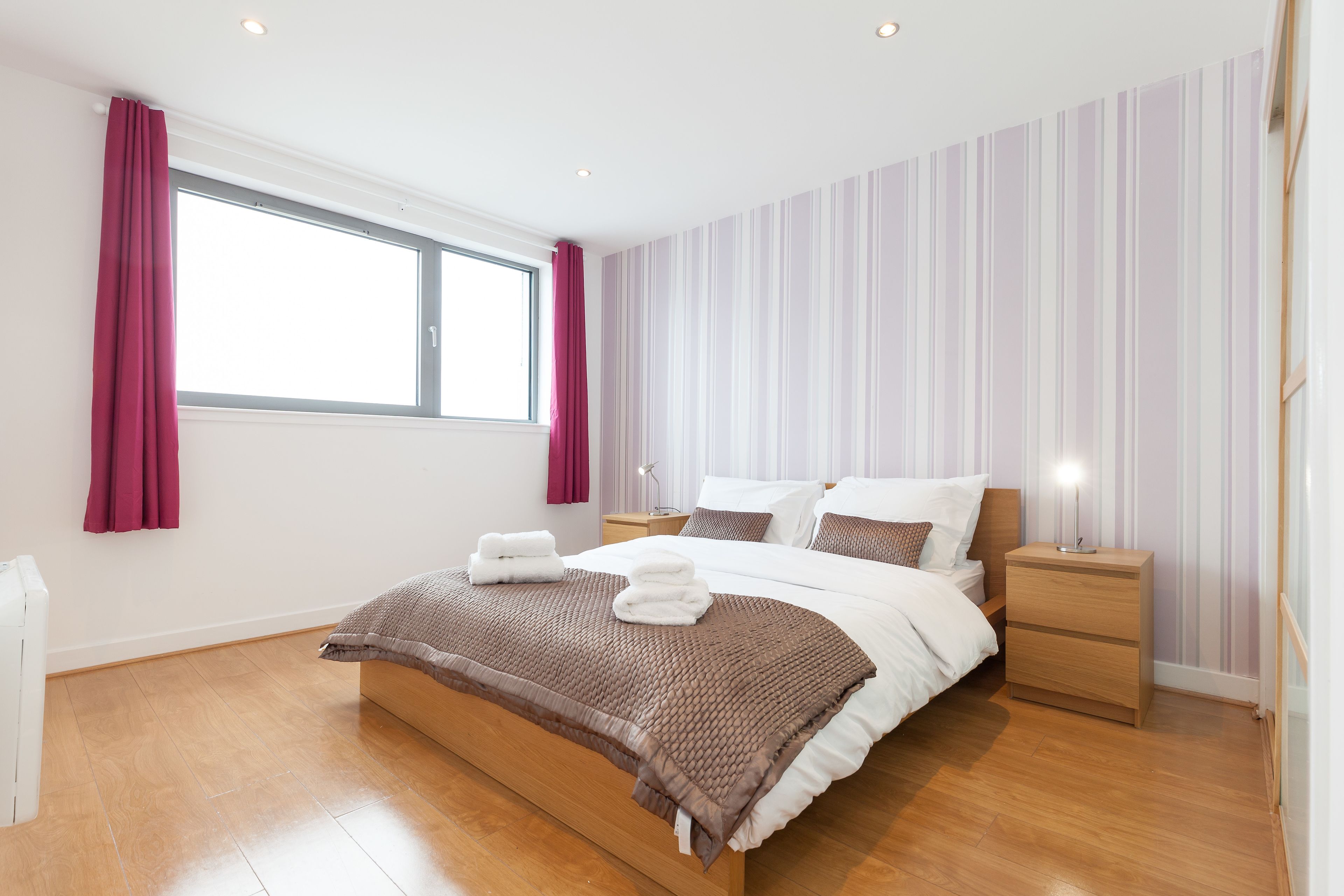 A bedroom with a large bed, wooden headboard, two bedside tables, a nightstand, and a window with curtains.