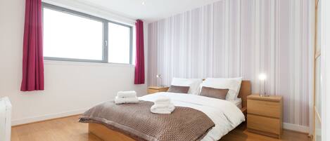 A bedroom with a large bed, wooden headboard, two bedside tables, a nightstand, and a window with curtains.
