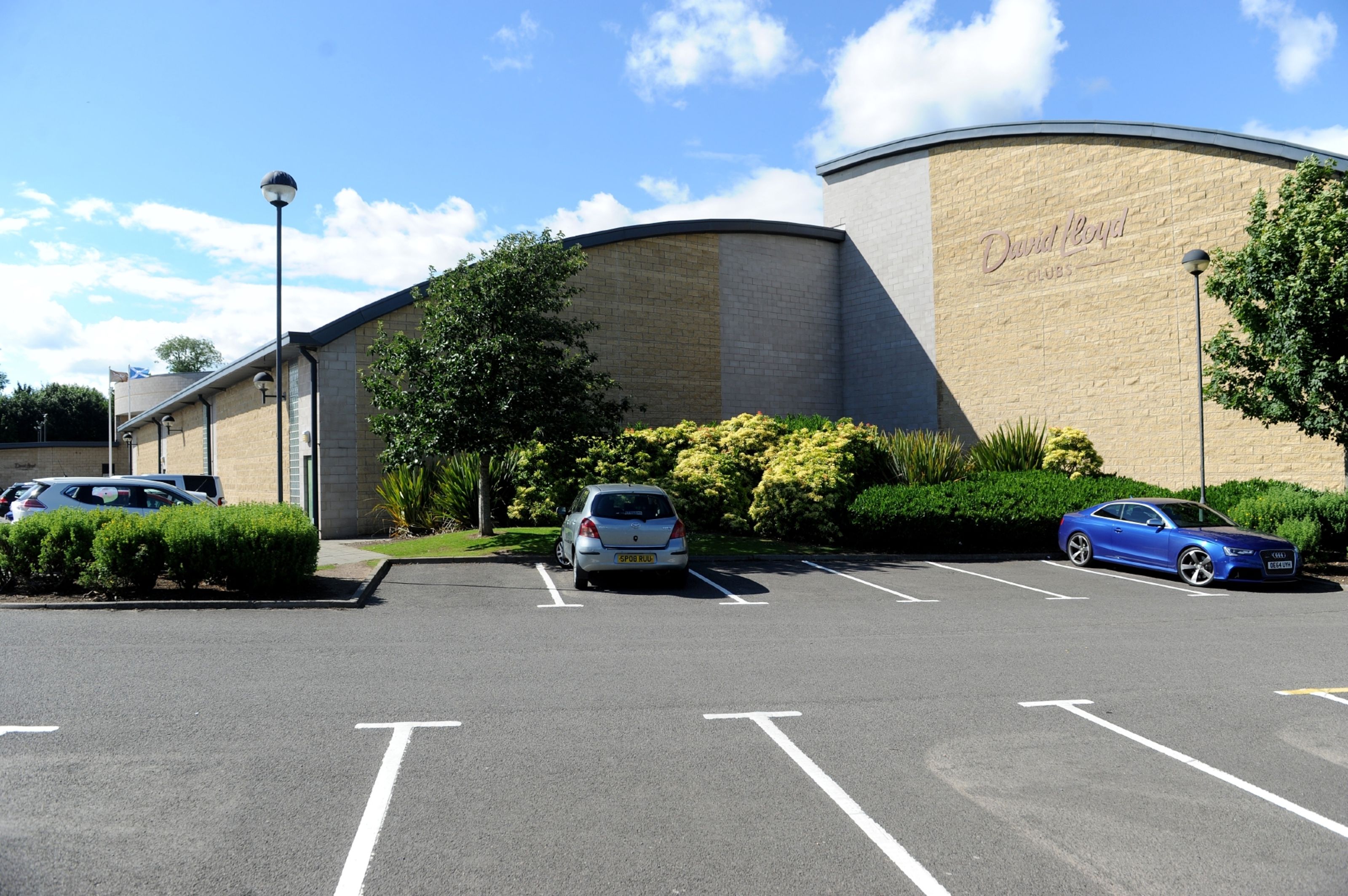 A parking lot with two cars, a building with "David Royal Clubs" signage, and a clear blue sky.