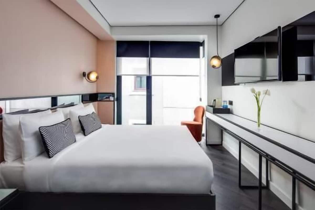 Habitación de hotel moderna con una cama grande, un pequeño rincón de descanso, una kitchenette y vistas a través de un ventanal.
