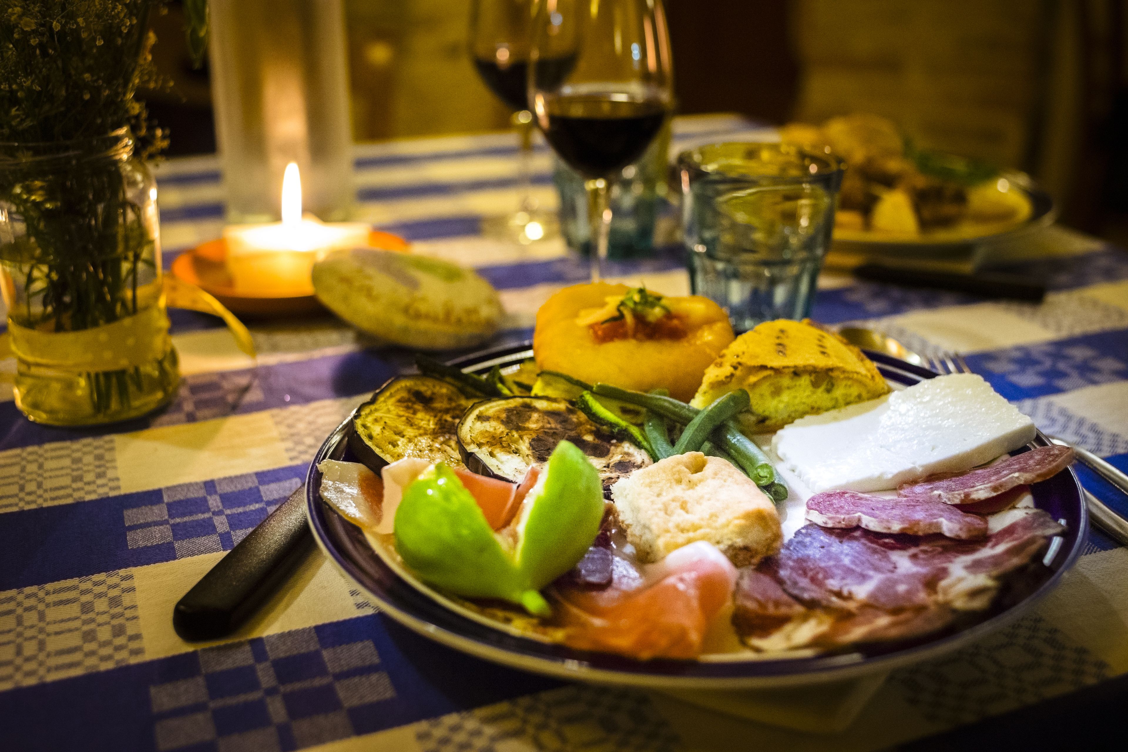 A table with a checkered tablecloth, a plate of food, a candle, and glasses of wine.