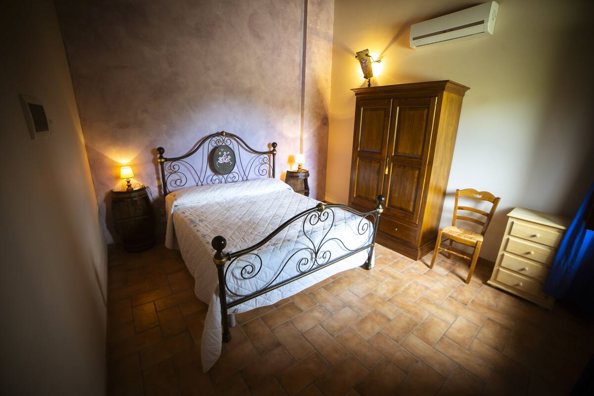 A bedroom with a bed, a wooden wardrobe, a chair, and a dresser.