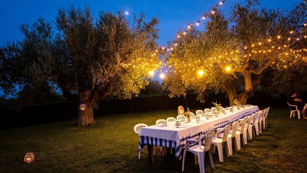 An outdoor dining setup with a long table, white chairs, and string lights. - Zà Culetta (Rocca San Giovanni)