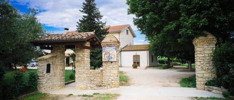 Un portail en pierre avec une enseigne, un bâtiment doté d’un toit en tuiles et un chemin menant à l’entrée.
