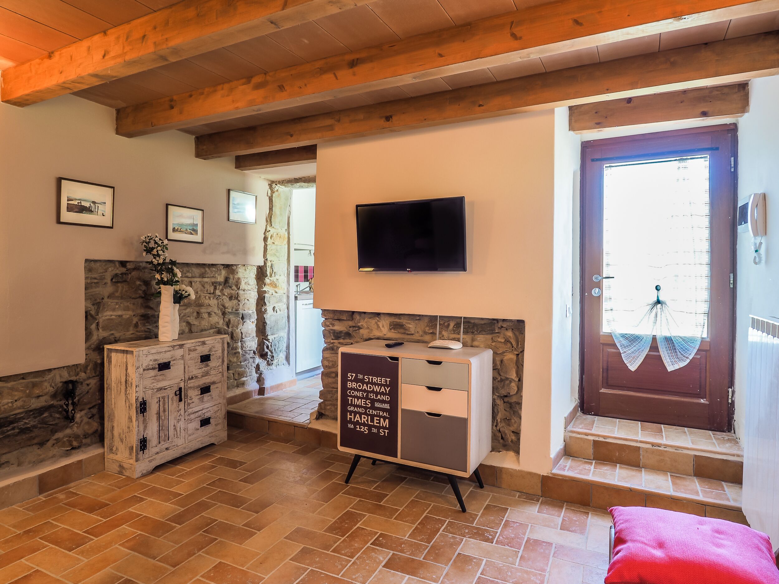 A room with a stone wall, a wooden cabinet, a television mounted on the wall, and a sign indicating the location.
