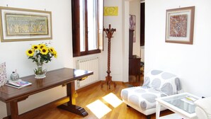 Un salon avec un plancher en bois, un canapé blanc, une table basse en verre, un bureau en bois et un vase rempli de tournesols.