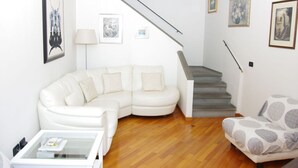Un salon avec un canapé d’angle blanc, une table basse en verre, un fauteuil à motifs et un escalier doté d’une rampe grise.