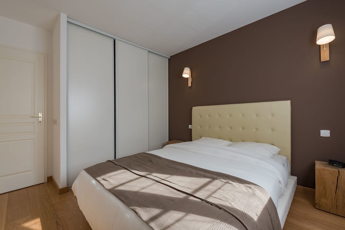 A bedroom with a bed, a wardrobe, and two wall-mounted lights.