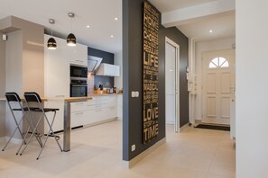A modern kitchen with white cabinets, stainless steel appliances, and two bar stools. - B&B House in Disneyland (Chanteloup)
