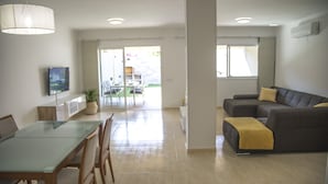 A modern living room with a glass dining table, a dark grey sofa, and a yellow throw blanket. - Luxury Villa in Maspalomas, Jacuzzi, Wifi, Pool, Parking (Maspalomas)