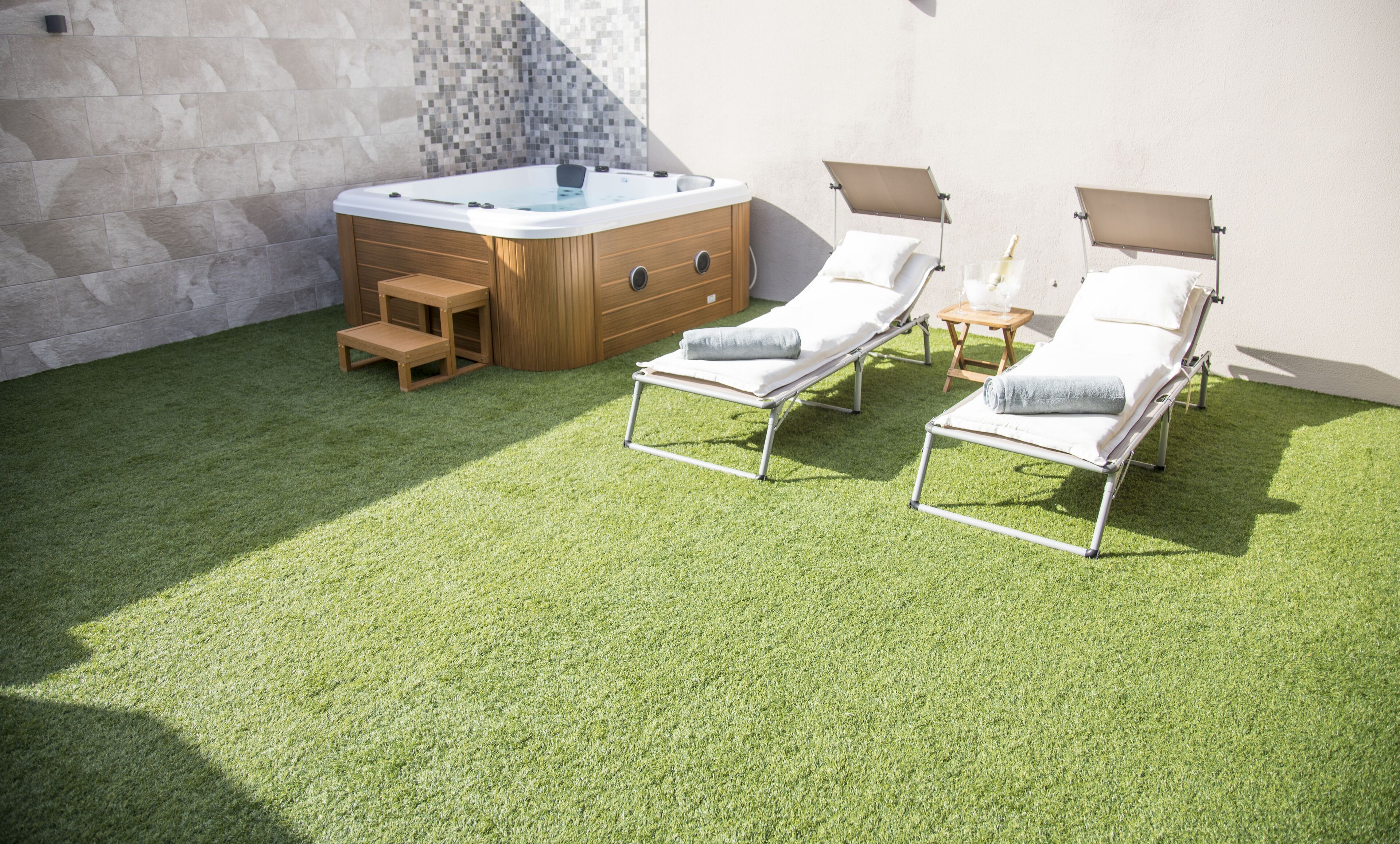 Un espace bien-être comprenant un bain à remous, deux chaises longues et un banc en bois.