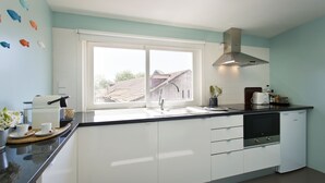 A modern kitchen with white cabinets, a black countertop, a stainless steel range hood, and a window with a view of a house outside. - Family Matters | Historic Center (Porto)