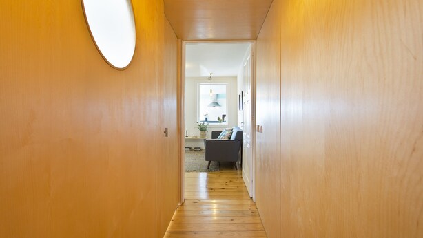 A wooden hallway leading to a room with a bed, a window, and a plant. - Family Matters | Historic Center (Porto)