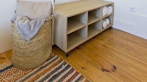 A room with a wooden floor, a woven basket with a towel, a striped rug, and a wooden bench with shelves. - Family Matters | Historic Center (Porto)