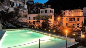 Una piscina con muelle de madera y vista a edificios escalonados al anochecer.