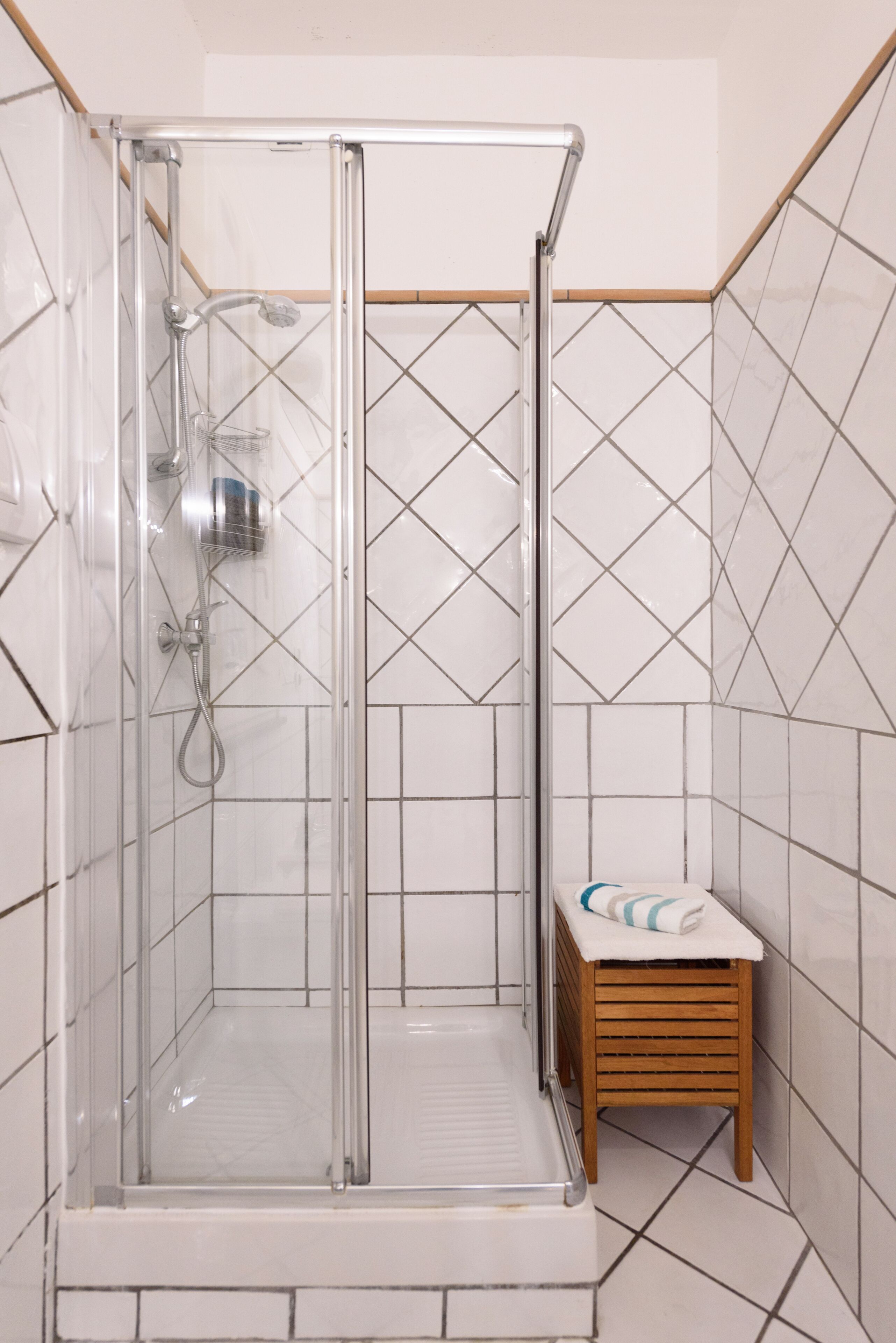 A glass-enclosed shower with a wooden stool and a towel.