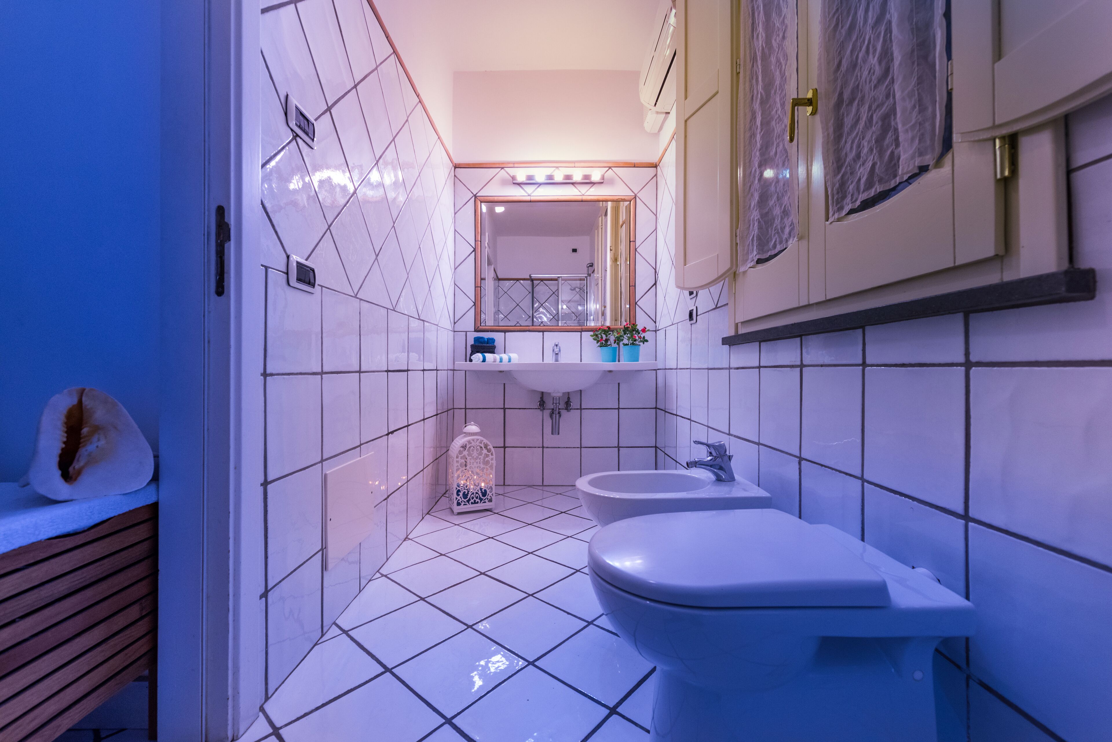 A bathroom with white tiles, a sink, a bidet, and a mirror.