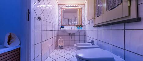 A bathroom with white tiles, a sink, a bidet, and a mirror.