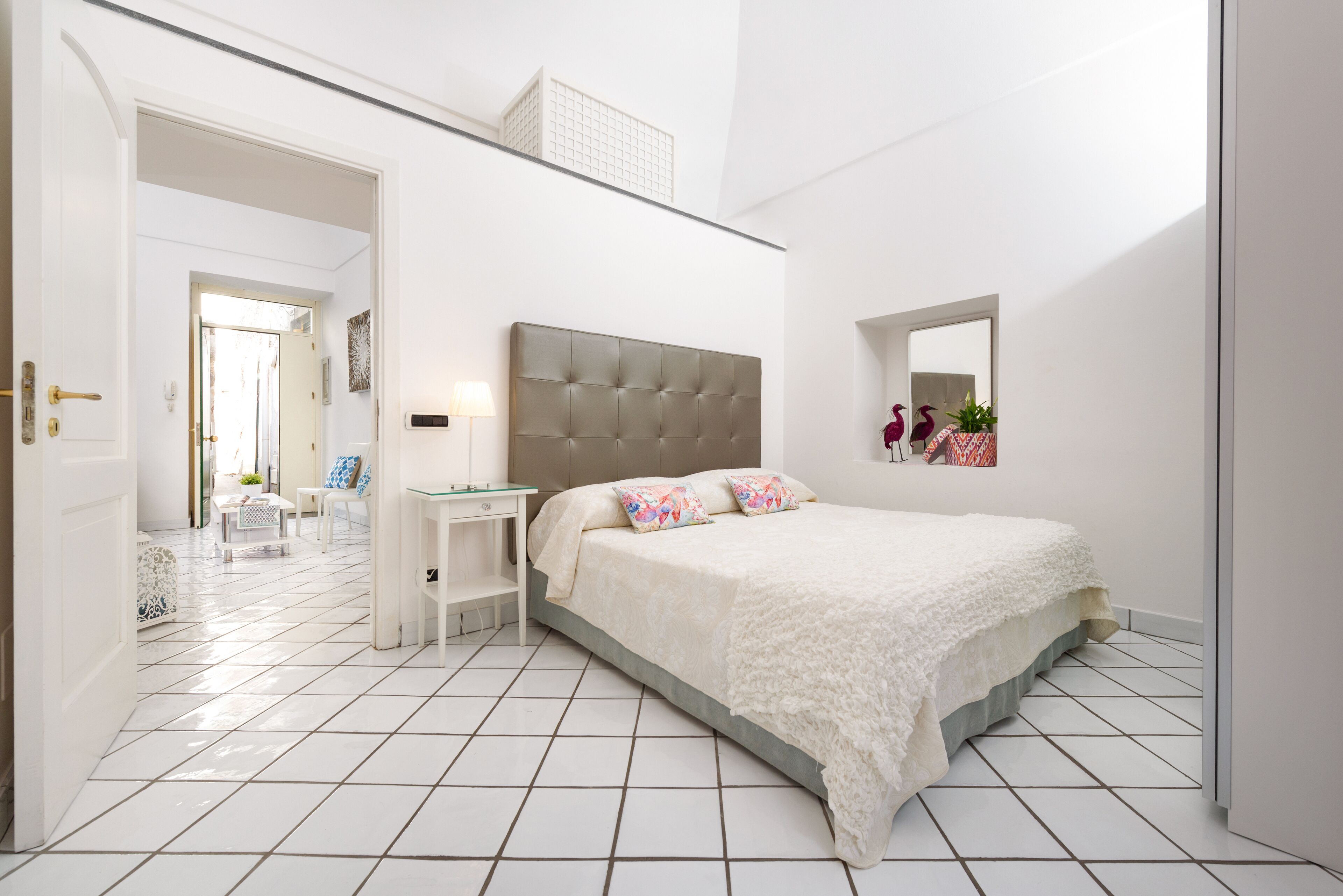 A bedroom with a large bed, a bedside table, a chair, and a mirror on the wall.