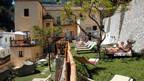 Un patio con sillones de descanso, un muro de piedra y un edificio con varios balcones.