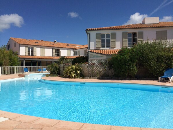 A swimming pool with a tiled deck, surrounded by a white fence and blue lounge chairs. - Bright and charming duplex apartment in pool residence, 100m from the beach (La Couarde-Sur-Mer)