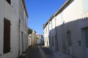A narrow street lined with white buildings with green shutters, a cobblestone path, and a clear blue sky. - Bright and charming duplex apartment in pool residence, 100m from the beach (La Couarde-Sur-Mer)