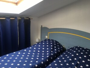A bedroom with a bed featuring a star-patterned bedspread, a headboard with a yellow accent, and a skylight above. - Bright and charming duplex apartment in pool residence, 100m from the beach (La Couarde-Sur-Mer)