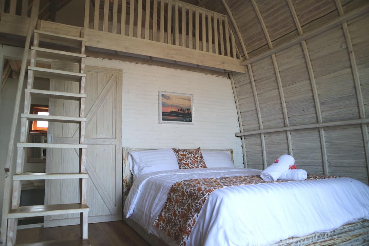 A bedroom with a wooden ladder, a bed with white bedding, and a painting on the wall.