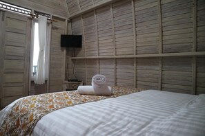 Une chambre d’hôtel avec un lit, un téléviseur fixé au mur et une fenêtre avec des rideaux.