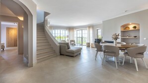 A spacious living area with a staircase, a dining table with chairs, and a large window providing natural light.