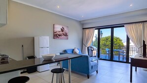 A modern kitchen with a dining area, a blue sofa, and a large sliding glass door leading to an outdoor patio. - Ballito Bay holiday Apartment (Ballito)