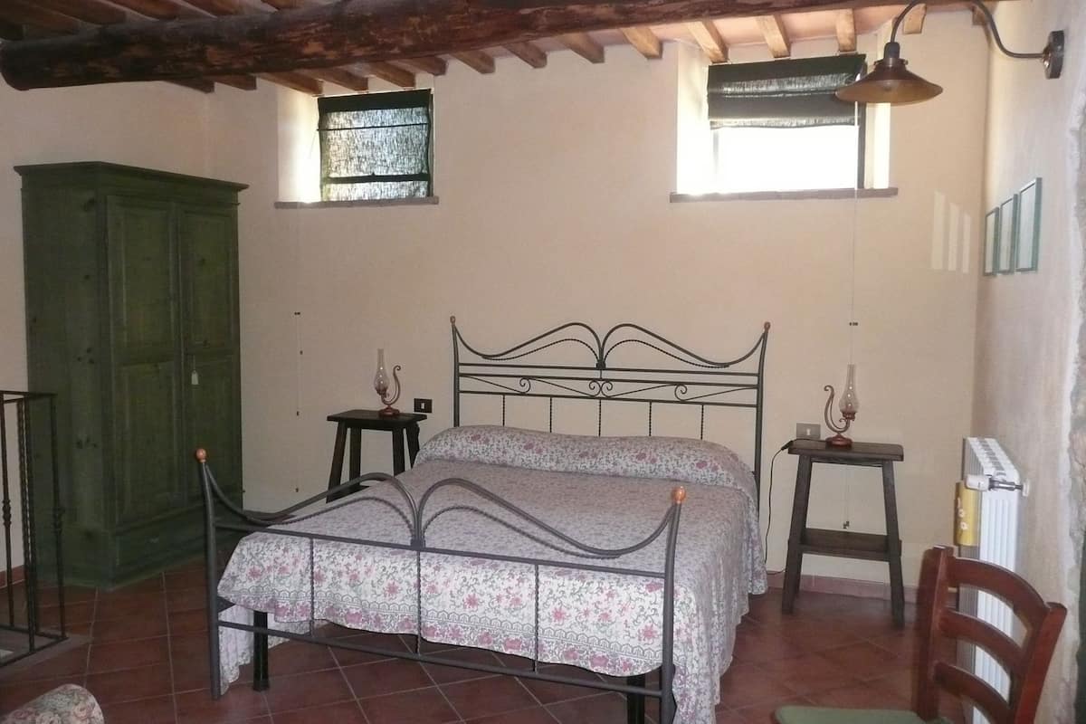 Quarto com cama, duas mesas de cabeceira, um guarda-roupa verde e uma janela.
