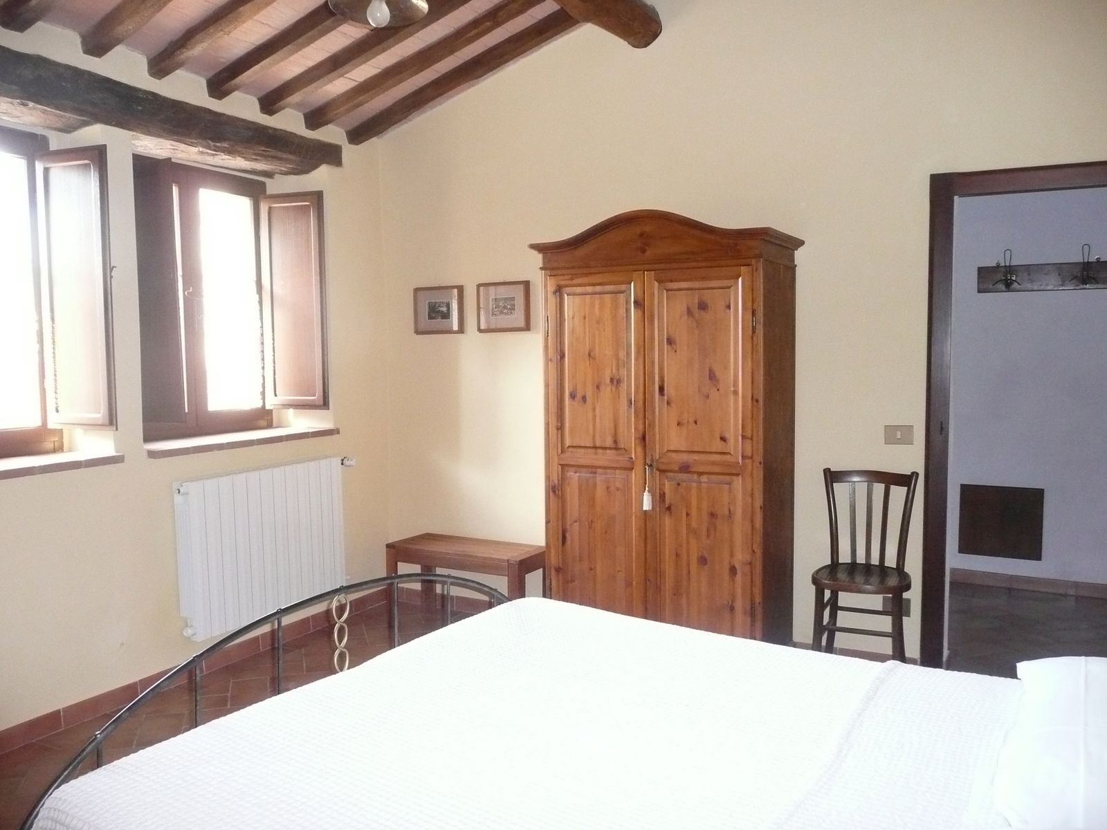 A room with a bed, wooden wardrobe, a chair, and a radiator.