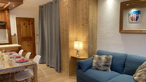 Un saló d'estar acollidor amb un sofà blau, una taula de dinar preparada per a quatre, parets de fusta i una làmpada sobre una taula auxiliar.