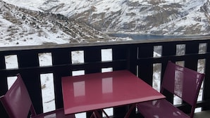 Un balcó amb taula i cadires vermelles amb vista a una muntanya coberta de neu i un llac.