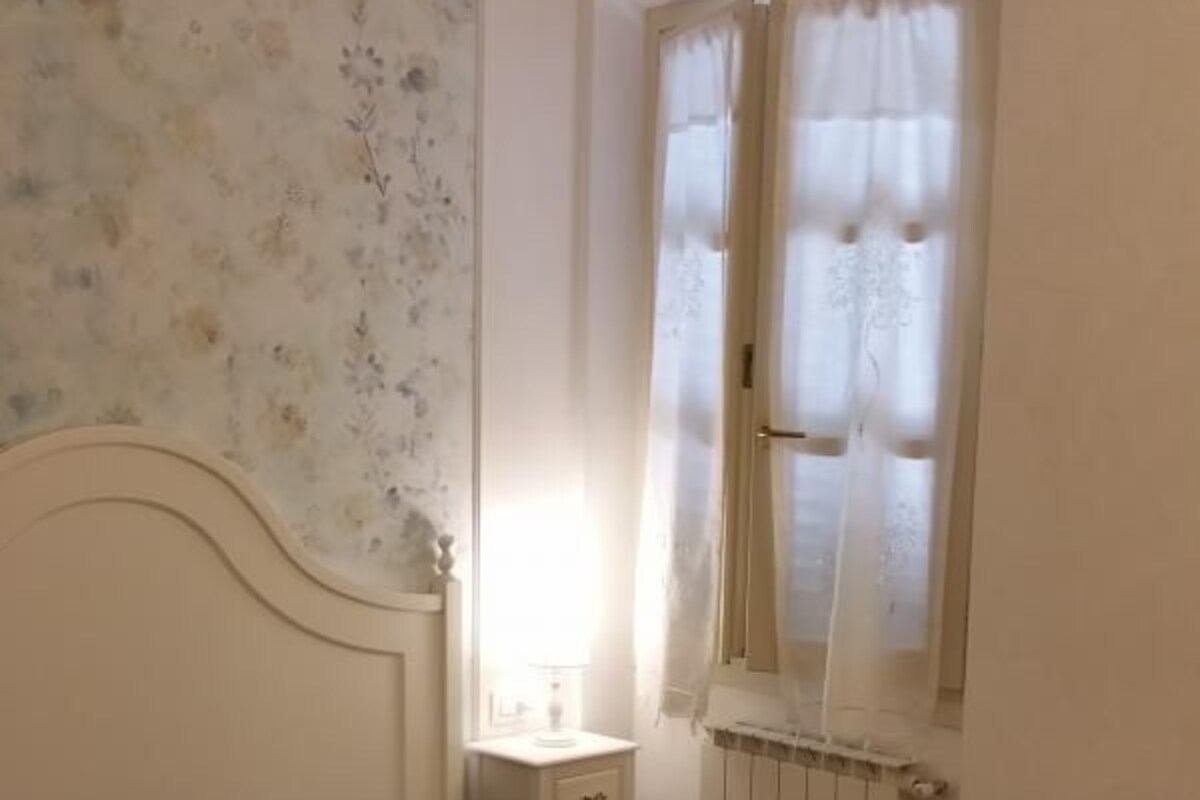 Een slaapkamer met een bed, een nachtkastje, een raam met gordijnen en een radiator.