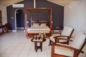 Un dormitorio con cama con dosel, una zona de estar con una mesa y sillas, y una pequeña mesa de comedor con una botella y copas.