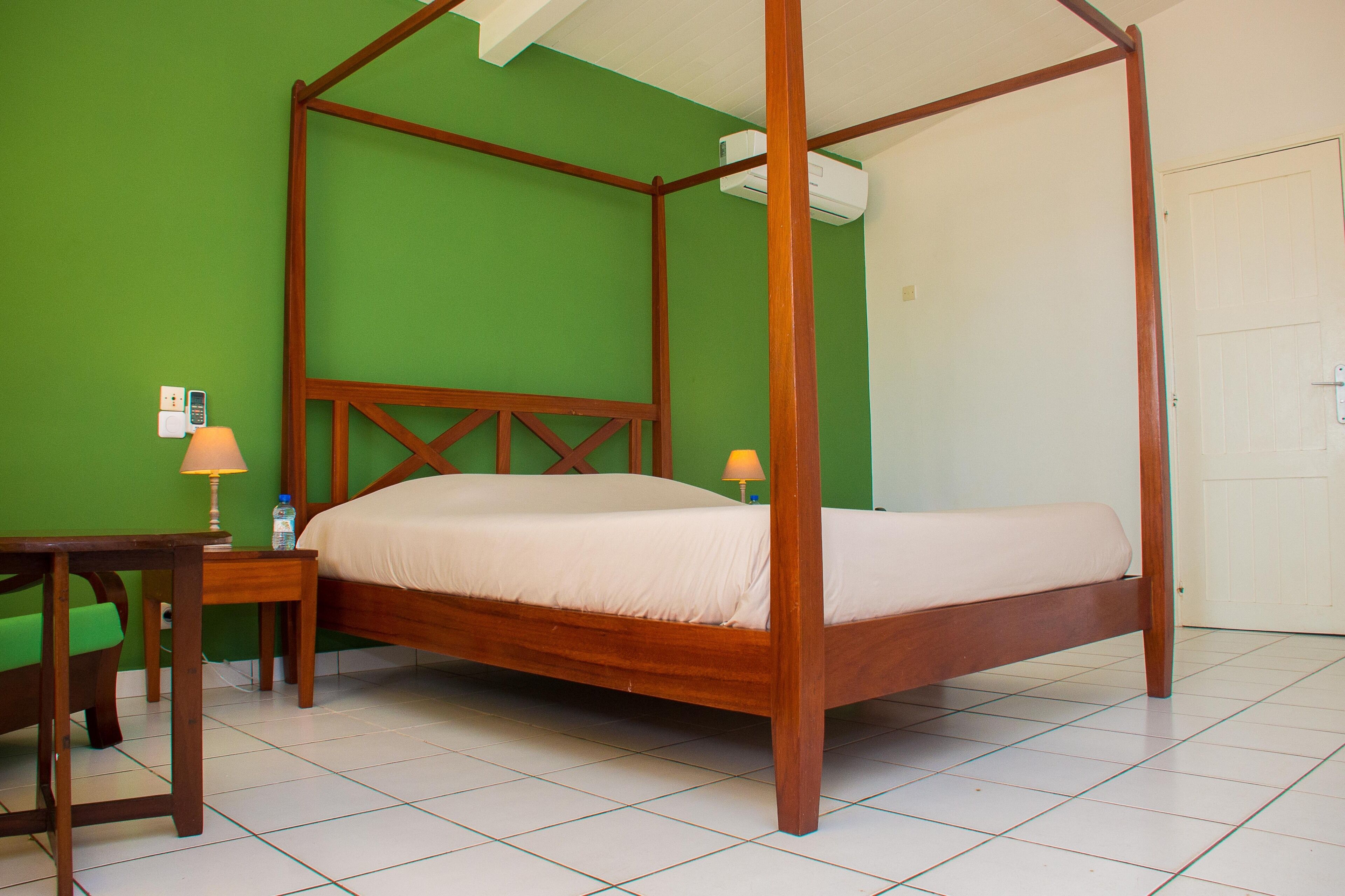 Una cama con dosel en una habitación con paredes verdes y suelo de baldosas blancas.