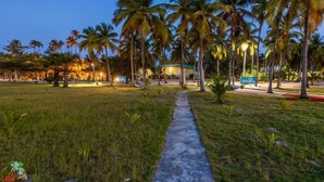 A pathway leading to a building with a blue roof, surrounded by palm trees and a grassy area. - Casa Del Papa Resort & SPA (Ouidah)