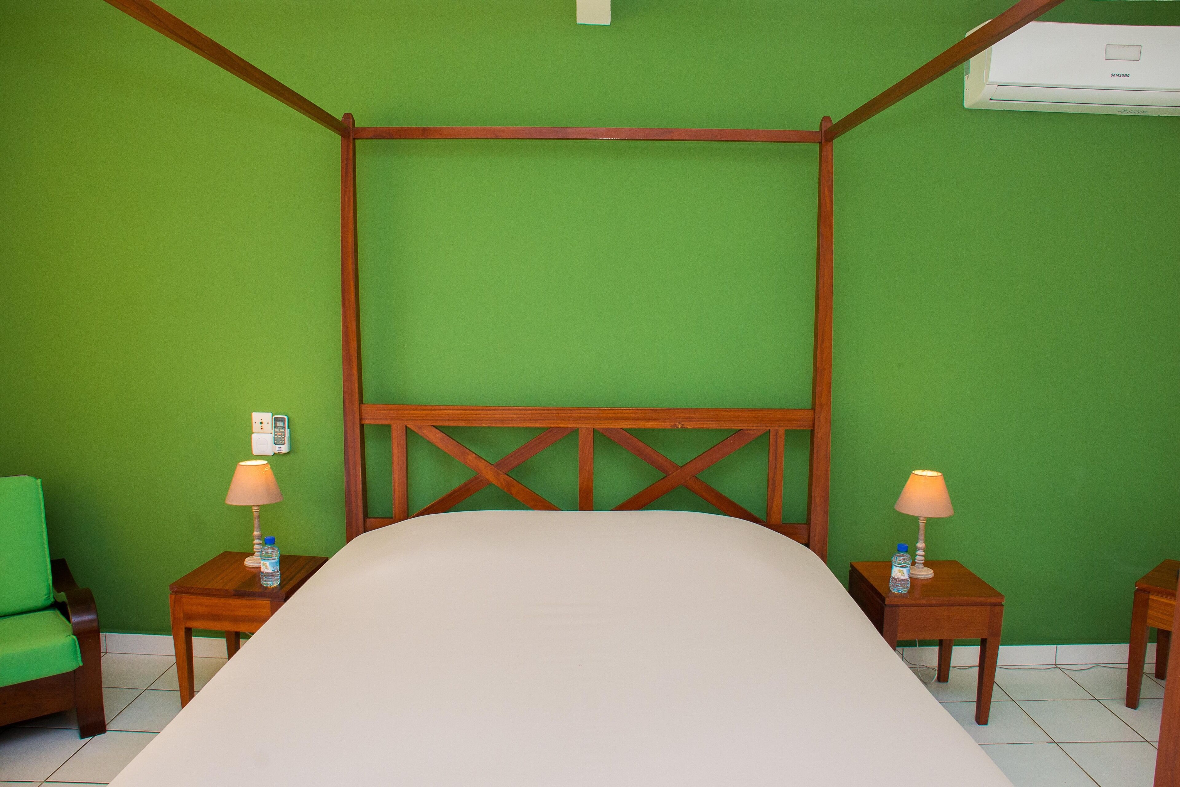 Una habitació amb un llit amb cortines, parets verdes, dues taules de nit amb làmpades i una cadira verda.