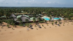 A resort with multiple bungalow-style buildings, a swimming pool, and a beach area with palm trees. - Casa Del Papa Resort & SPA (Ouidah)