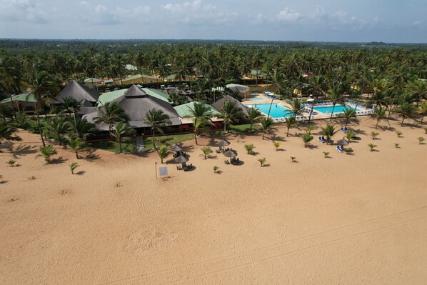 Un resort con varias construcciones tipo bungalow, piscina y zona de playa con palmeras.