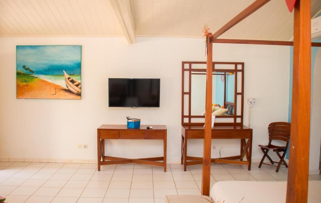 A room with a bed, a TV, a painting of a beach, a desk, and a chair.